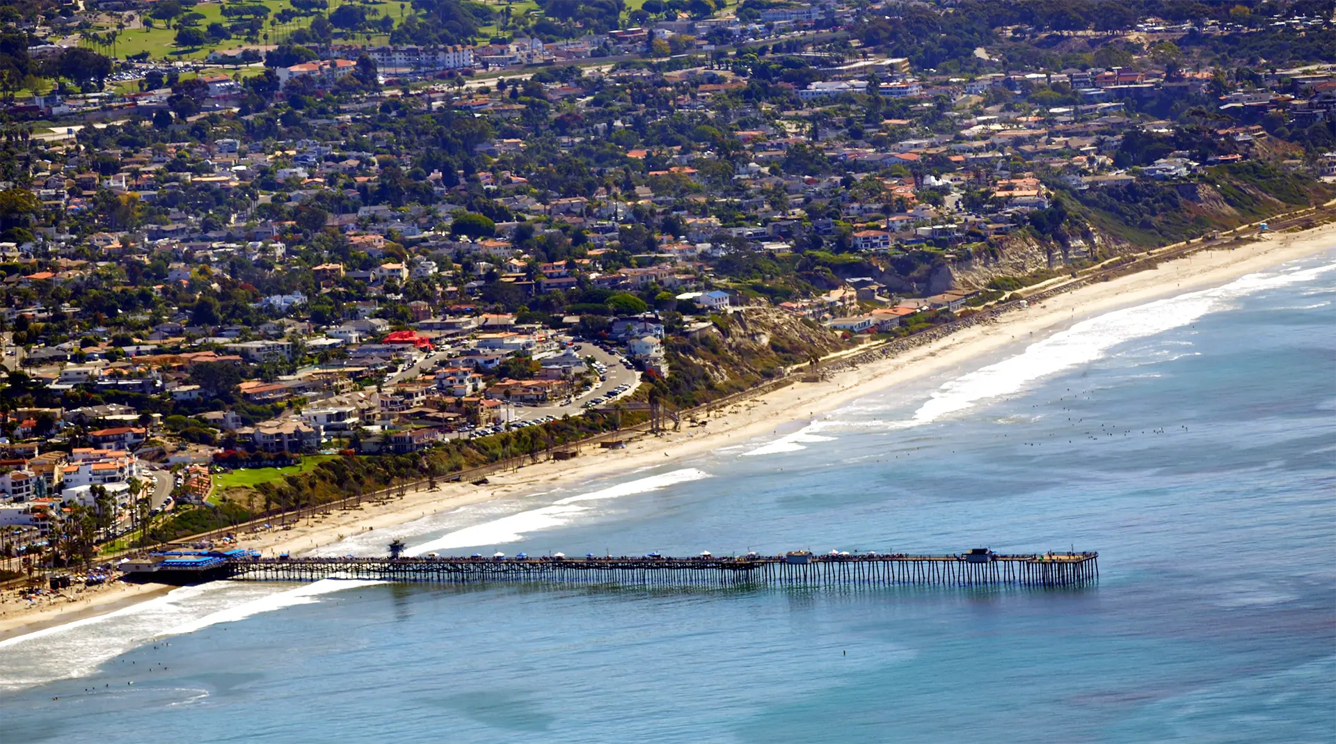 Coastal area with pier, beach, and houses on hill