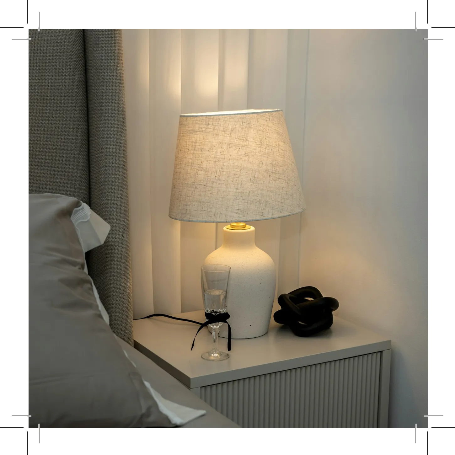 Bedside table with lamp, glass, and curtains